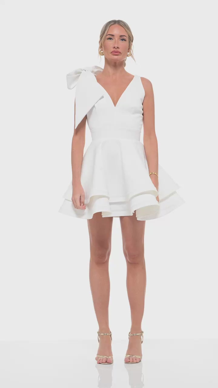Ivory bridal-inspired mini dress – RHOEN (ex-Rebecca Rhoades) designer gown with V-neckline, shoulder bow, and tiered skirt.
