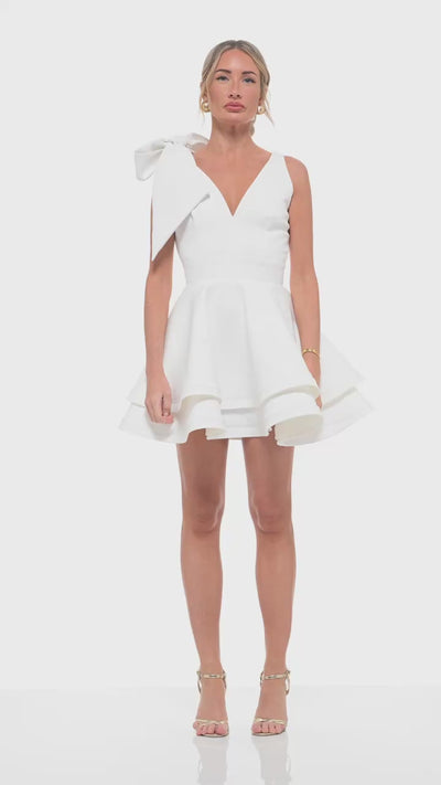 Ivory bridal-inspired mini dress – RHOEN (ex-Rebecca Rhoades) designer gown with V-neckline, shoulder bow, and tiered skirt.